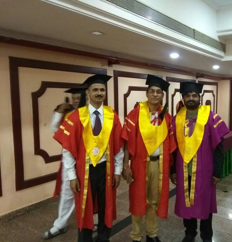 Three graduates in red convocation robes and yellow stoles at a PhD award ceremony